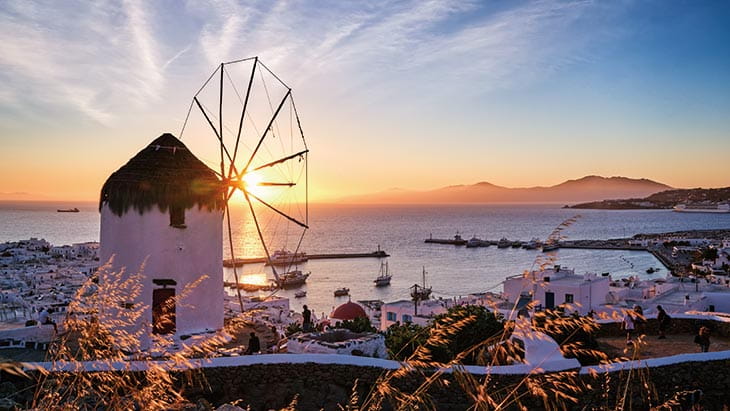 A view of a white windmill looking over the bay in Mykonos at sunset, Greece